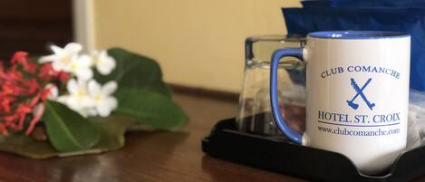 Eine weiße Tasse mit blauem Text und einem Logo, auf einem schwarzen Tablett zusammen mit einer Karaffe und einem Blumenstrauß.