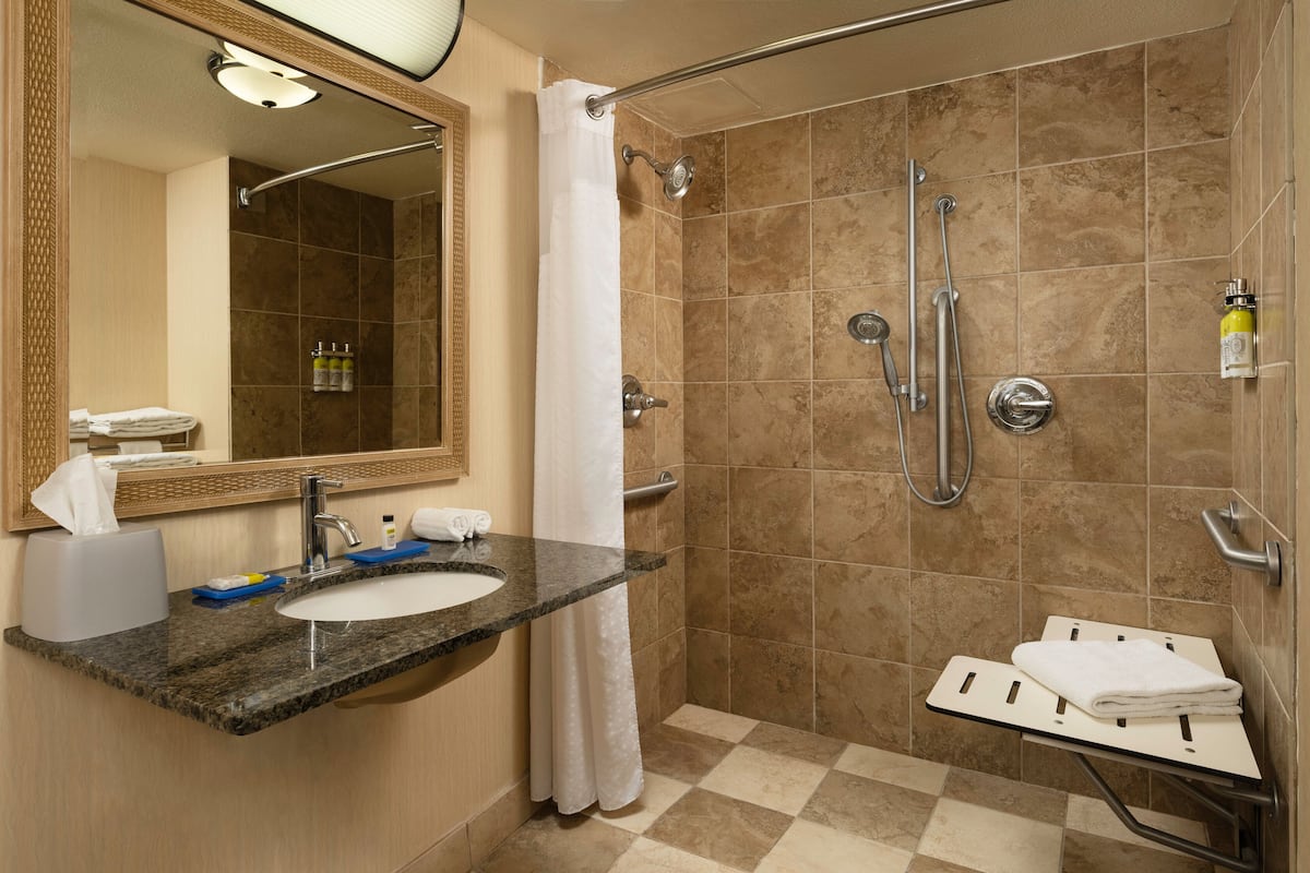 A bathroom with a granite countertop sink, a mirror, a shower with a handheld showerhead, and a glass-enclosed toilet.