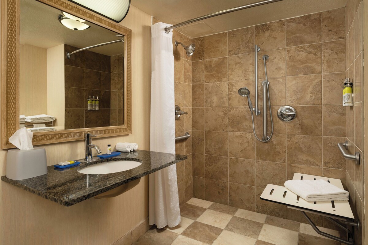 A bathroom with a sink, mirror, shower, and towel rack.