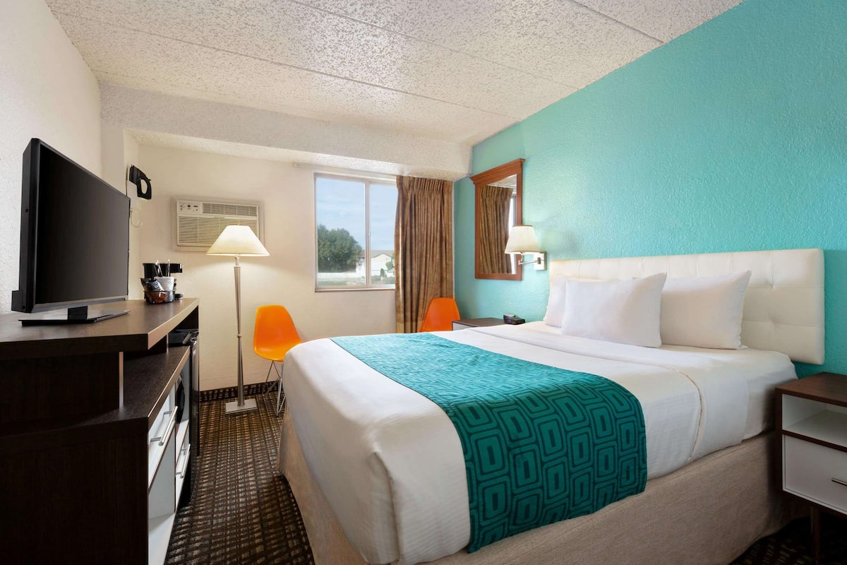 A hotel room with a bed, a TV, a desk, and a window with curtains.