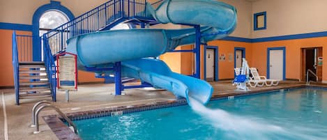An indoor swimming pool with a blue water slide and a staircase leading to a higher platform.