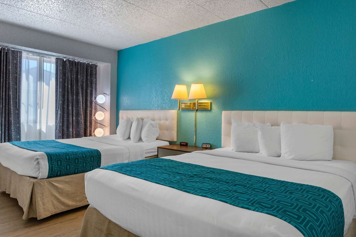 A hotel room with two beds, a teal accent wall, and a window with curtains.