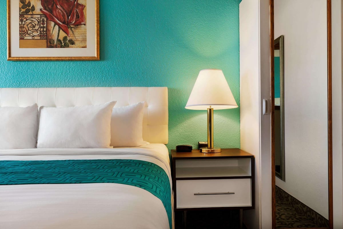 A hotel room with a bed, a nightstand, a lamp, and a framed picture on the wall.