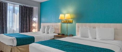 A hotel room with two beds, teal walls, and a nightstand with a lamp.