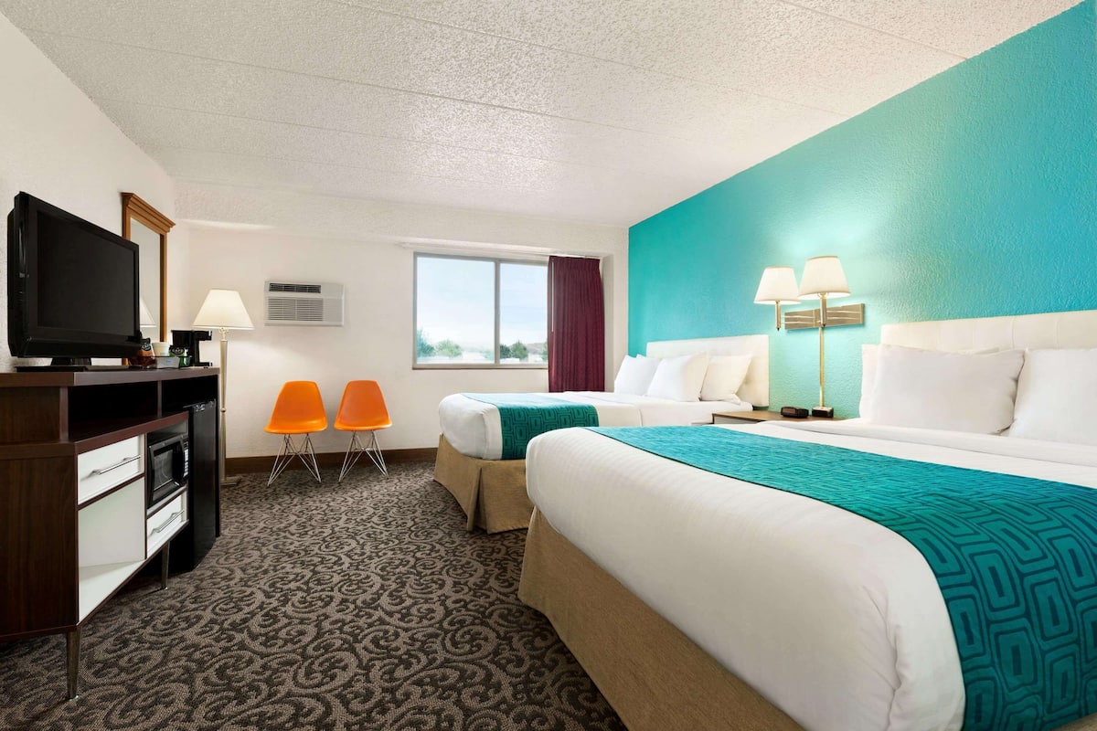 A hotel room with a bed, two chairs, a desk with a television, and a window.