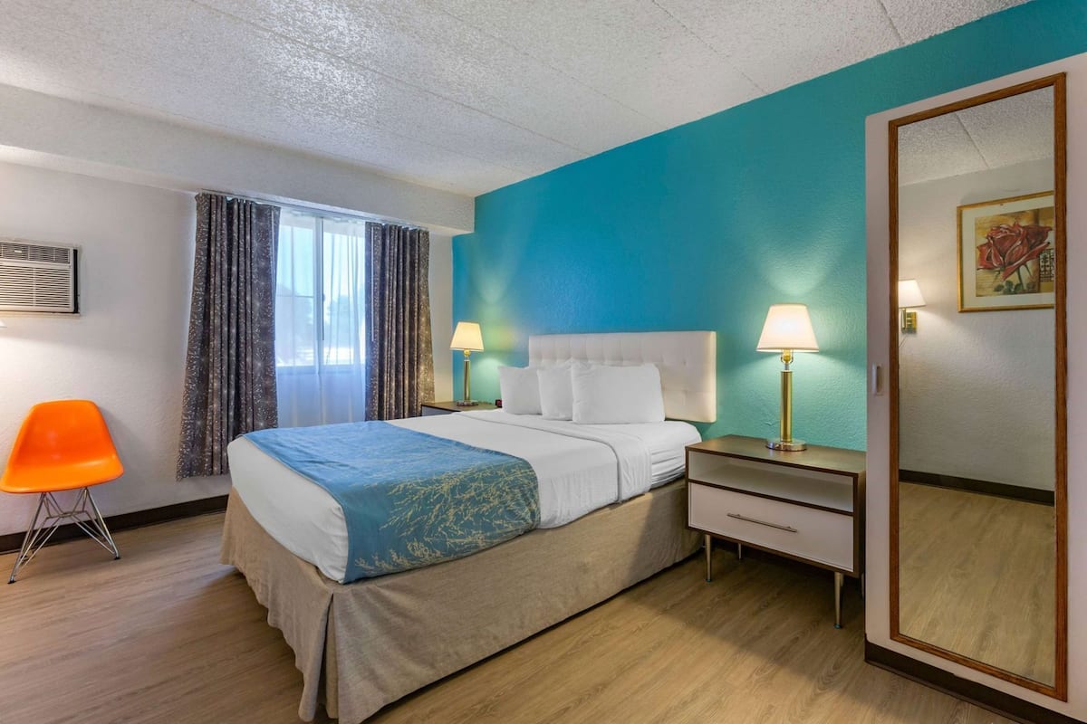A hotel room with a bed, a nightstand, a lamp, a chair, and a mirror.