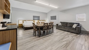 A modern hotel room with a dining area, a sofa, a bed, and a TV.
