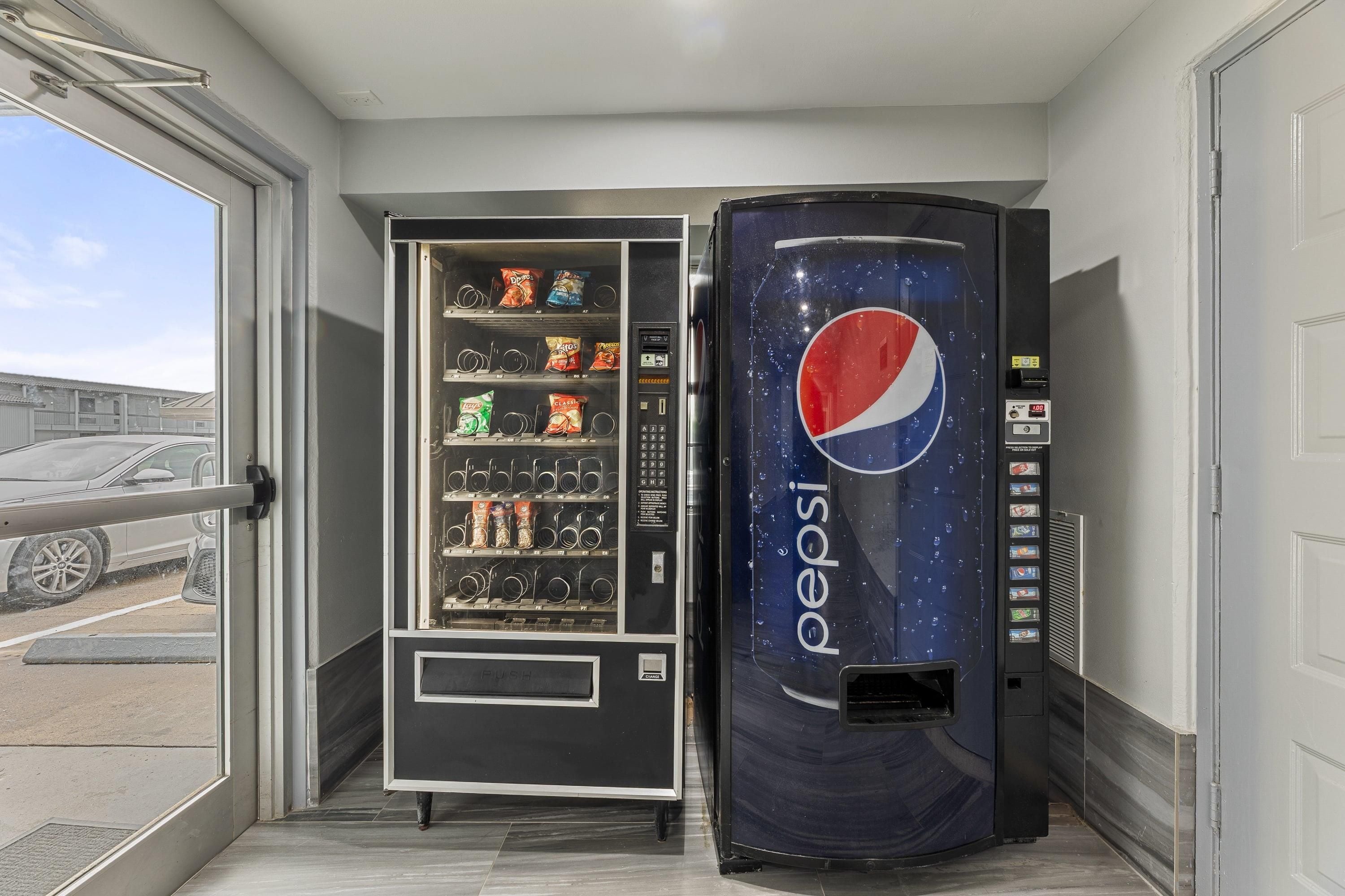 Un distributeur automatique orné du logo Pepsi, situé entre une porte et une fenêtre.
