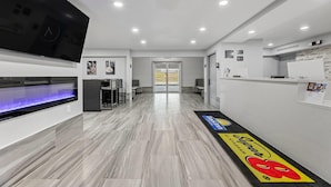 Un moderno vestíbulo de hotel con un mostrador de recepción, un televisor de pantalla plana, un acuario iluminado en azul y un área de recepción con un tapete con logotipo.