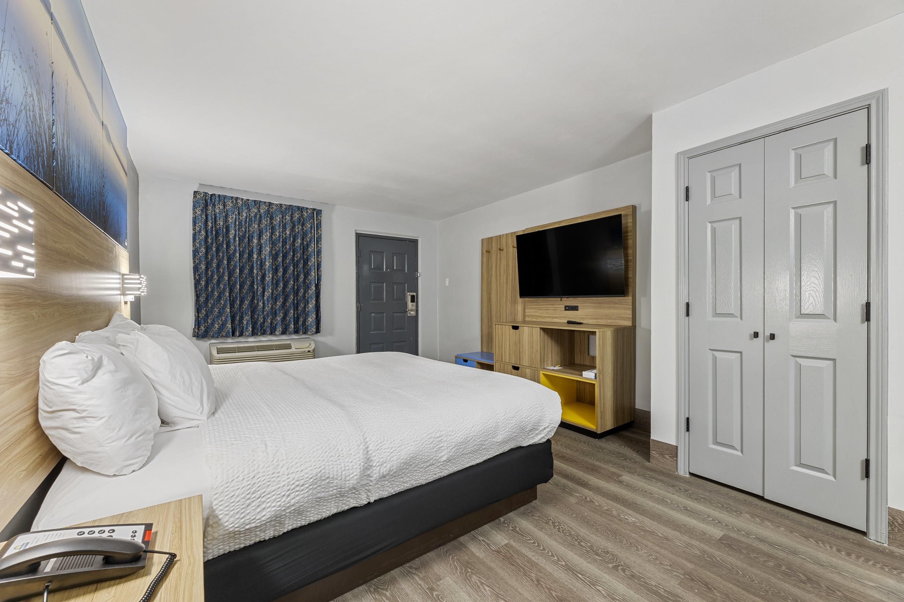 A hotel room with a bed, a television, a wardrobe, and a door.