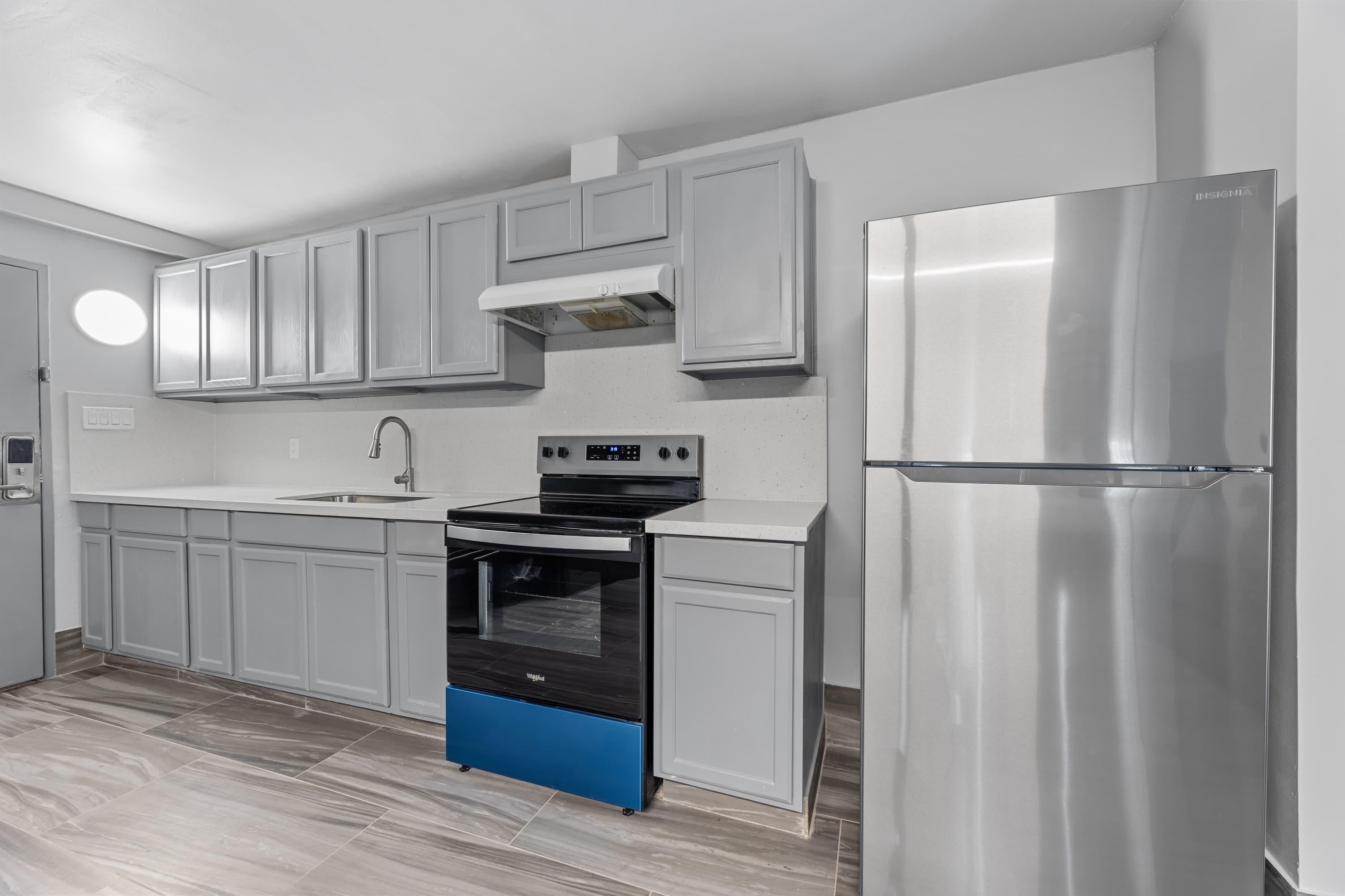 A modern kitchen with white cabinets, a stainless steel refrigerator, a black oven, and a blue dishwasher.