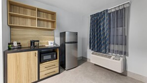 A compact kitchen with a built-in microwave, a refrigerator, and a window with patterned curtains.