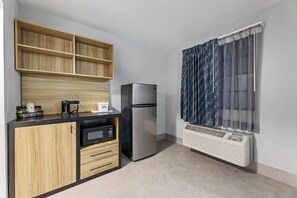 A compact kitchen with a built-in microwave, a refrigerator, and a window with patterned curtains.