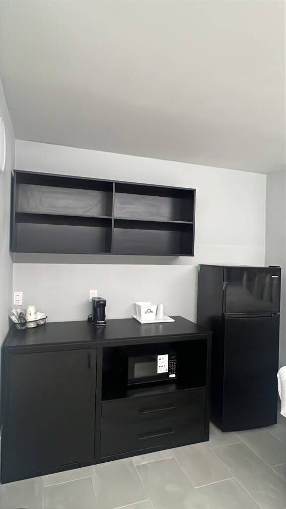 A kitchenette with a black countertop, a microwave, a coffee maker, and a refrigerator.