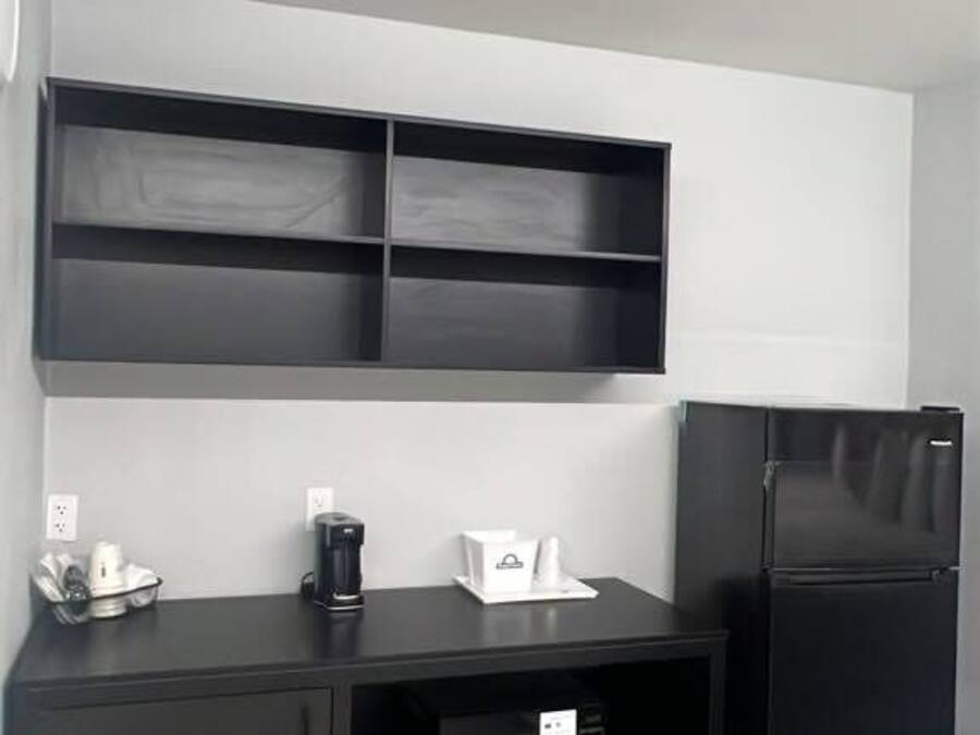 A kitchenette with a black countertop, a microwave, a coffee maker, and a refrigerator.