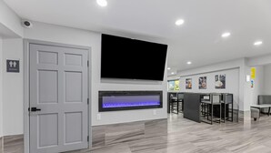 Un interior moderno con un televisor de pantalla plana sobre la chimenea, una puerta con la leyenda 'Baño' y una zona de bar con asientos.