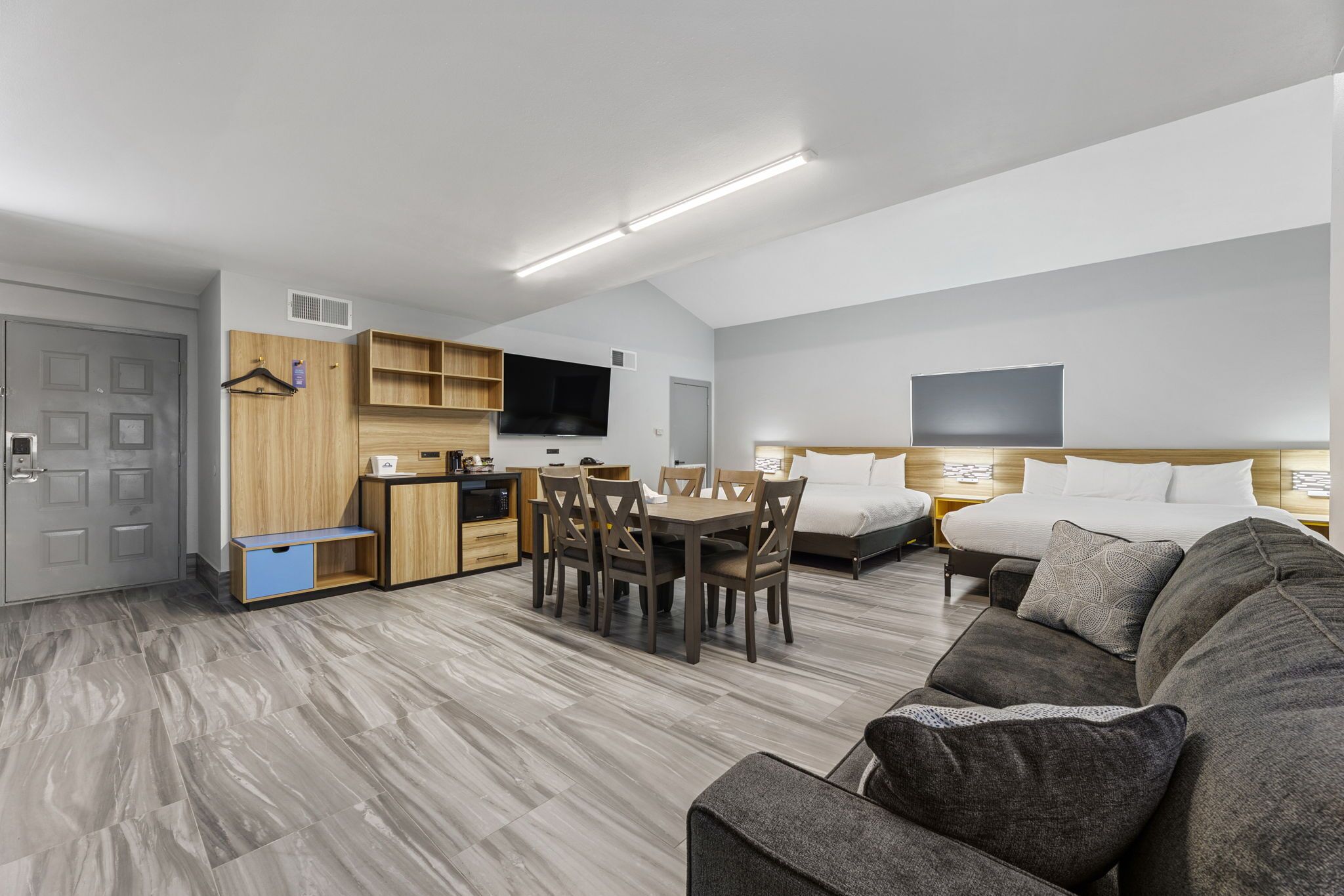 Una habitación de hotel moderna con comedor, kitchenette y una cama grande con cabecera.