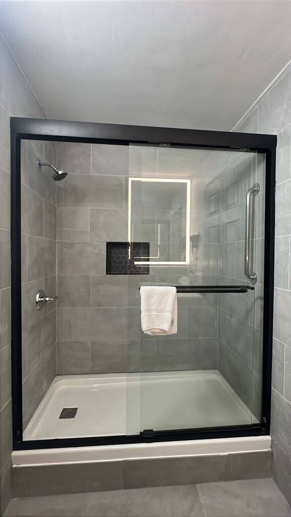 A glass-enclosed shower with a white towel hanging on a rack, a glass shower door, and a small rectangular mirror on the wall.