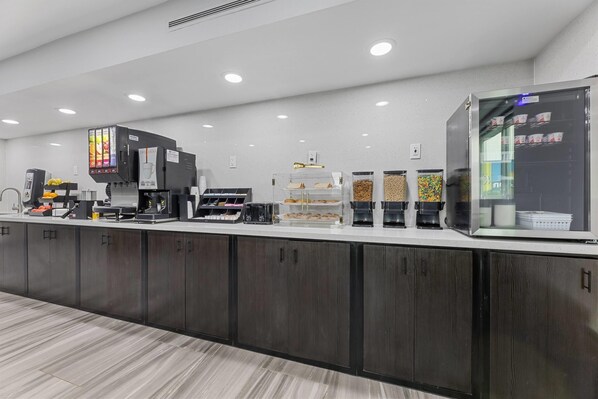 A modern coffee station with multiple coffee machines, a refrigerated display case, and various coffee pods and containers.