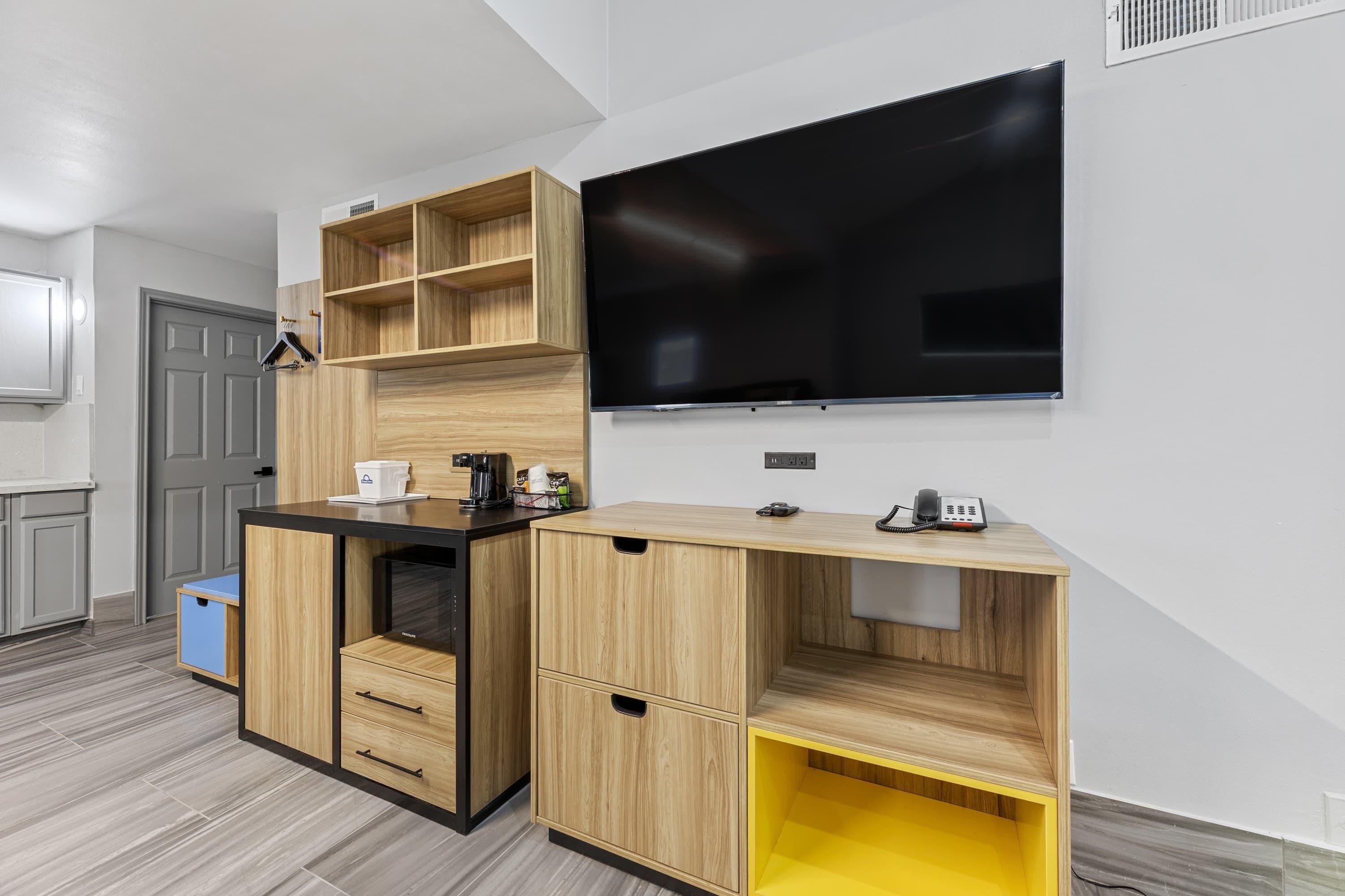 A modern kitchen with built-in wooden cabinets, a black countertop, and a large flat-screen TV mounted on the wall.