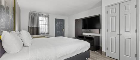 Una moderna camera d'albergo con un letto, una scrivania, una TV a schermo piatto e un armadio.