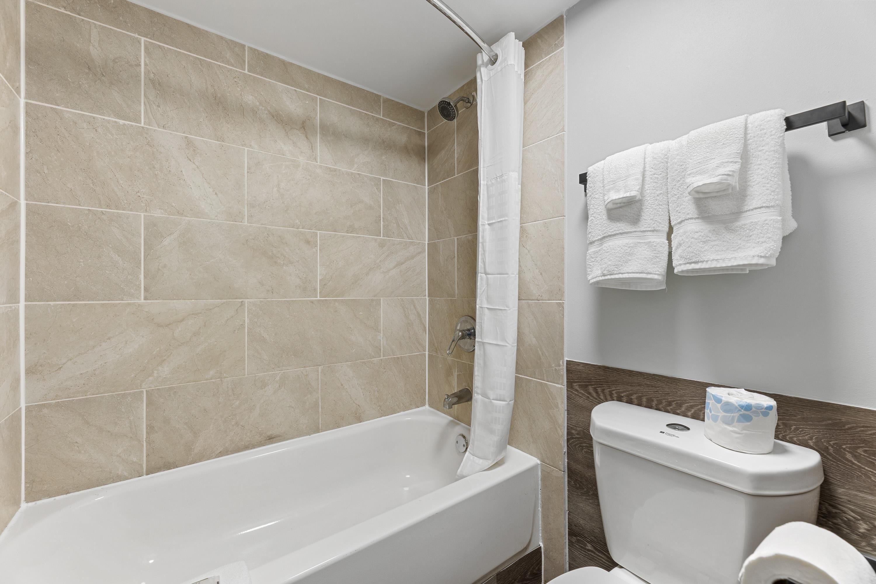 A bathroom with a bathtub, a shower curtain, a toilet, and a towel rack with towels.