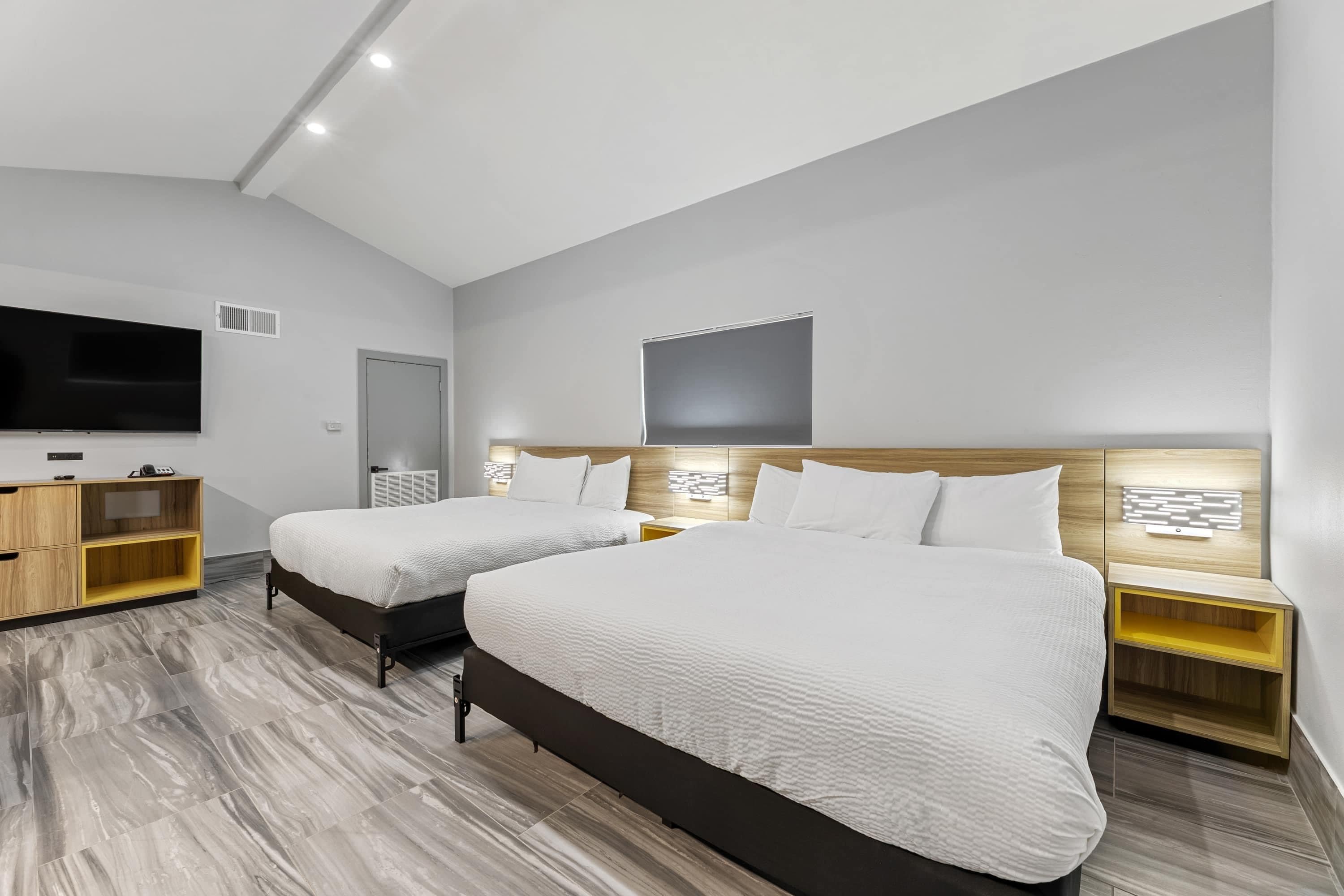 Habitación de hotel moderna con dos camas, televisor e iluminación empotrada.