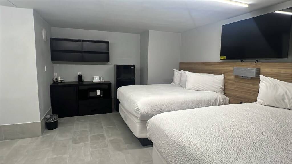 A hotel room with two beds, a flat-screen TV, a small desk with a coffee maker, and a trash bin.