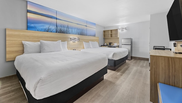 Una habitación de hotel con dos camas, un escritorio, un televisor y una obra de arte grande en la pared.