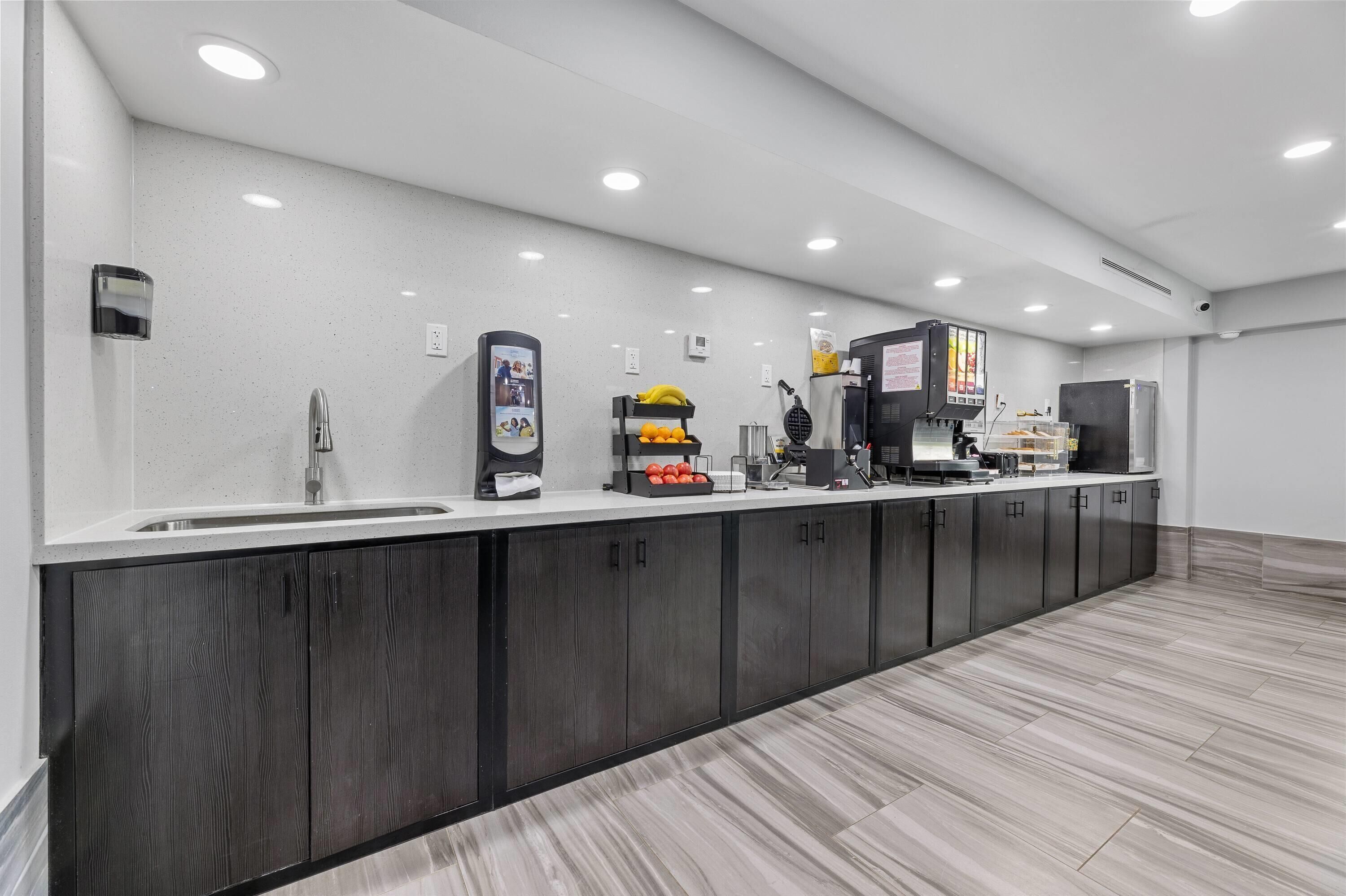 A modern kitchen with a long counter, built-in cabinets, and a variety of appliances including a coffee machine and a waffle maker.