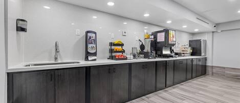 A modern kitchen with a long counter, built-in cabinets, and a variety of appliances including a coffee machine and a waffle maker.