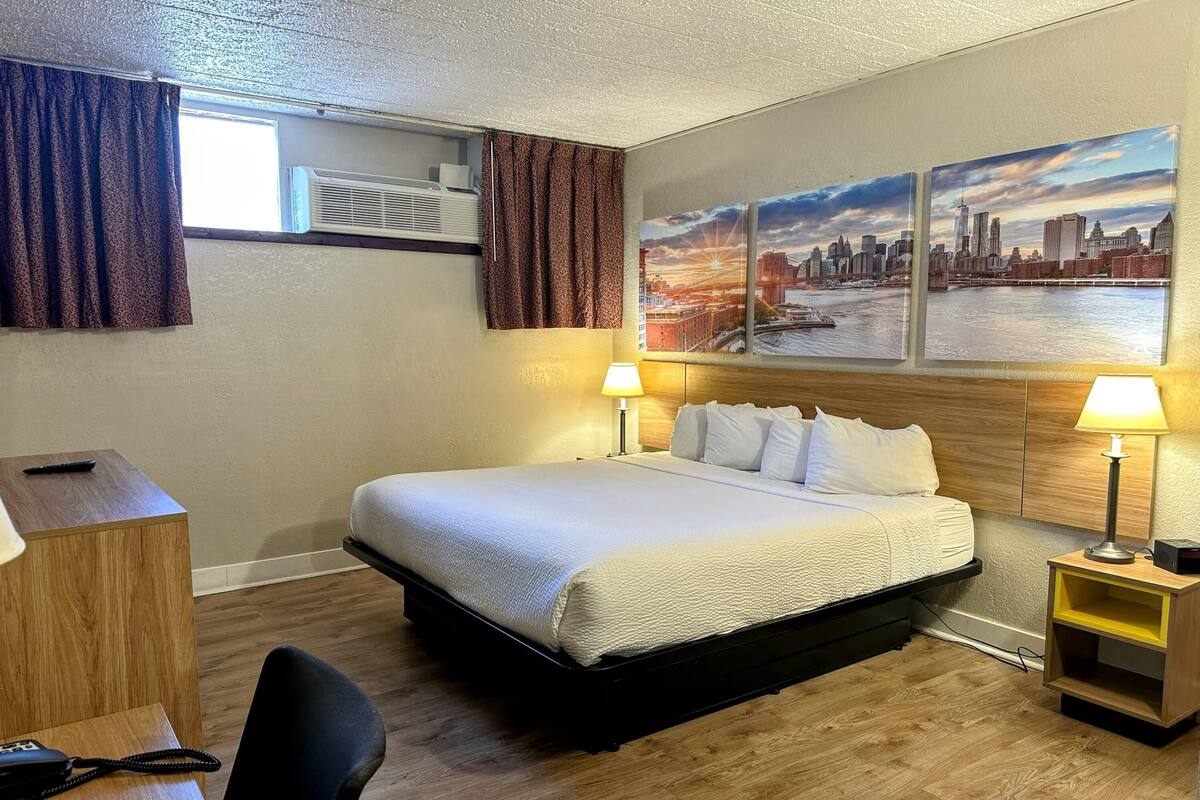 A hotel room with a bed, bedside lamps, a desk with a telephone, a chair, and a window with curtains.