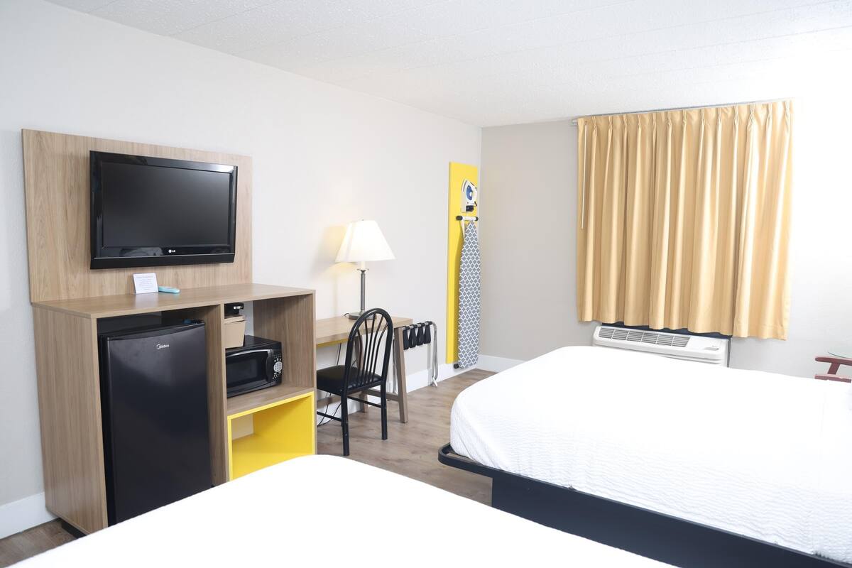 A hotel room with a bed, a desk with a computer, a television, and a refrigerator.