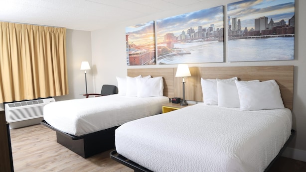 Une chambre d’hôtel avec deux lits, un bureau, une chaise, une lampe et un grand tableau représentant un paysage urbain accroché au mur.