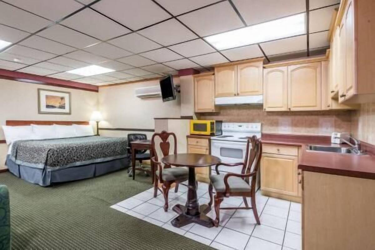A compact hotel room with a bed, a small dining table with chairs, a microwave, and a stove.
