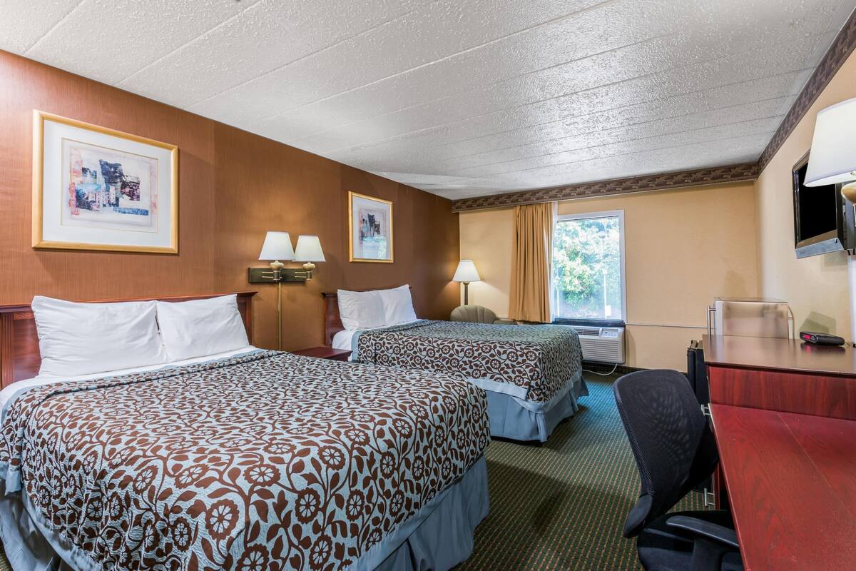 A hotel room with two beds, a desk, a chair, and a TV.