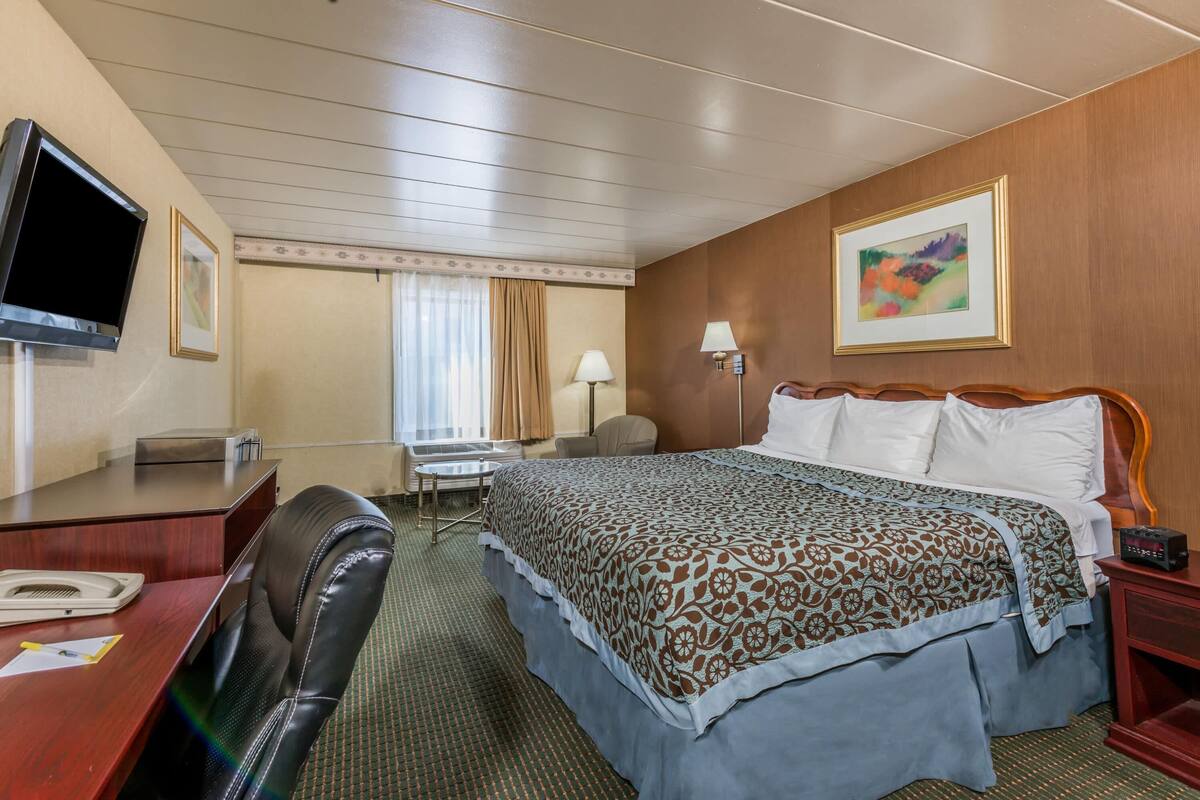 A hotel room with a bed, desk, chair, television, and artwork on the walls.