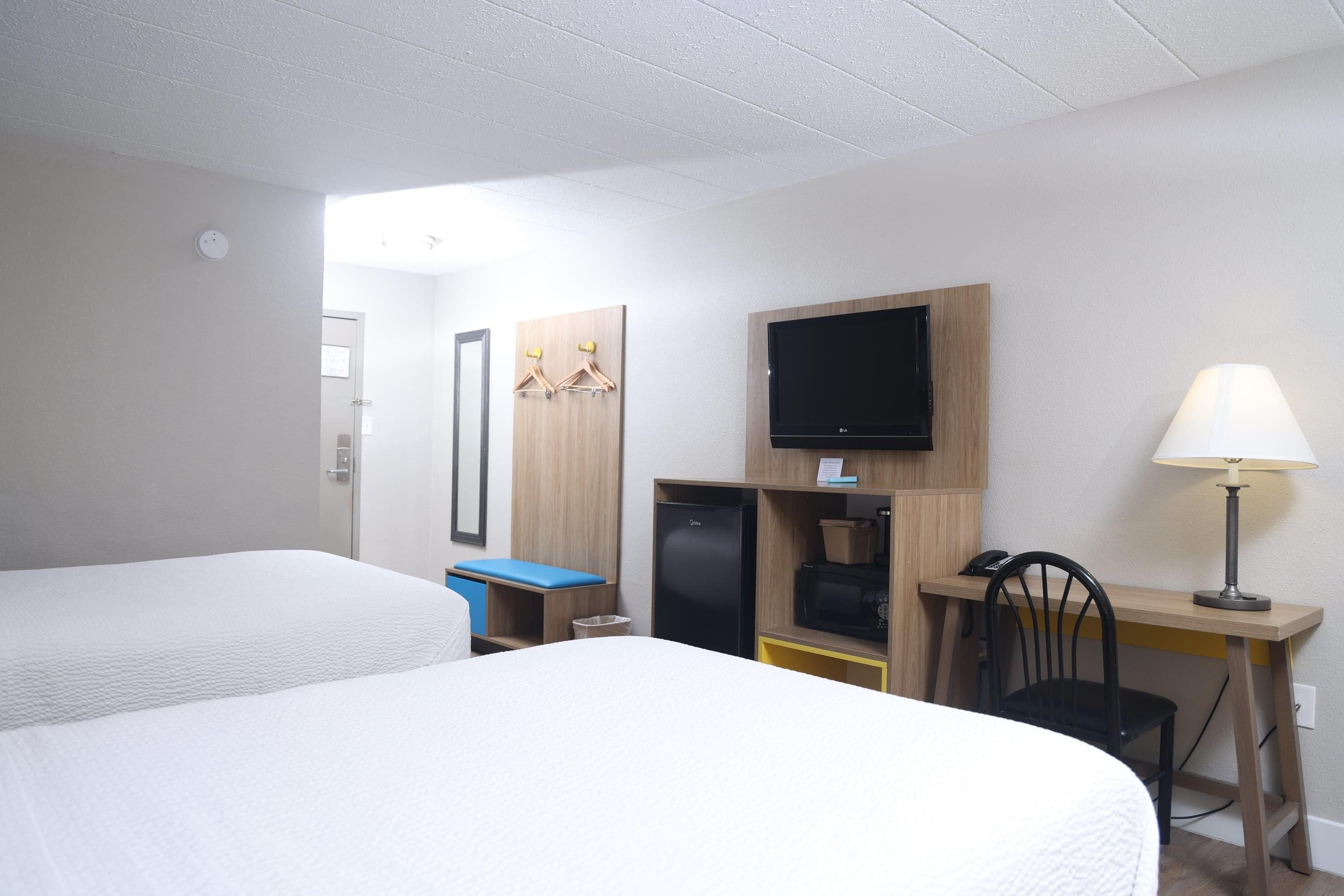 A hotel room with two beds, a desk with a computer, a television, and a lamp.