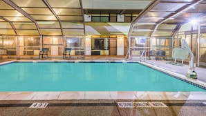 Une piscine couverte avec un toit en verre, des chaises longues et un panneau indiquant qu’il est interdit de plonger dans la zone peu profonde.