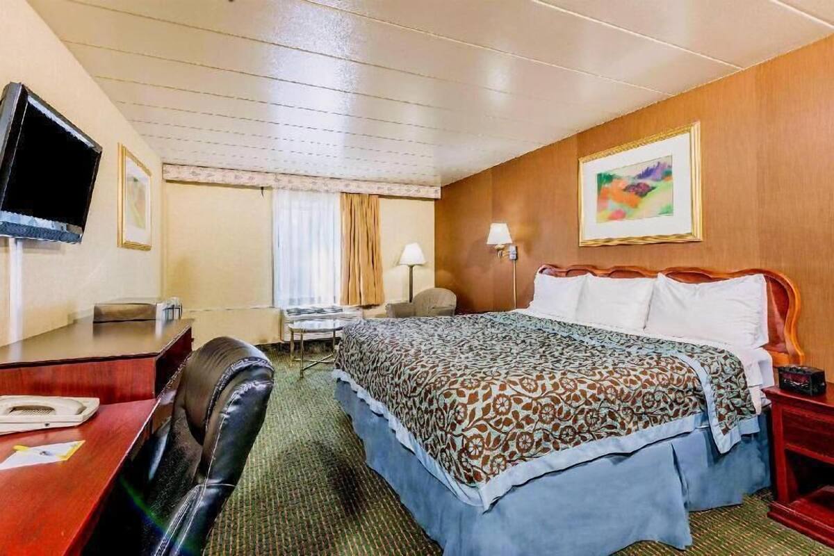 A hotel room with a bed, a desk, a chair, a television, and a painting on the wall.
