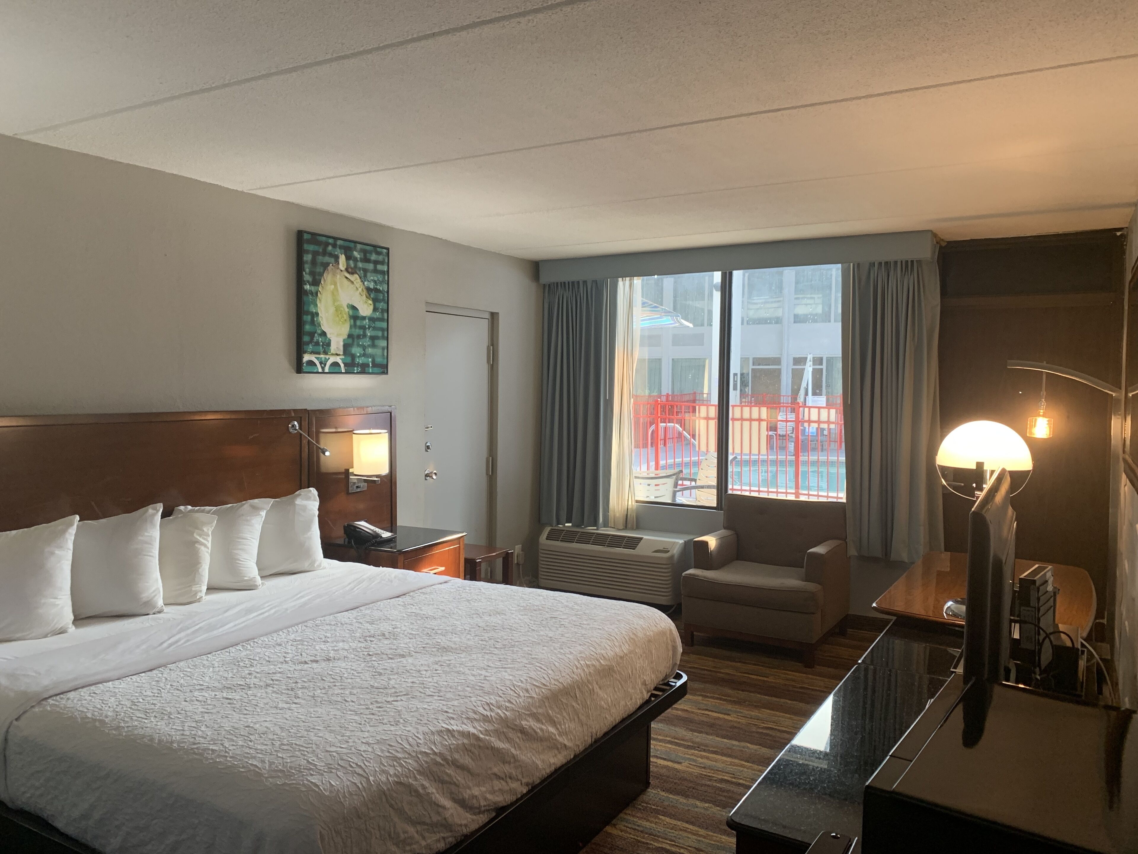 Hotellihuone, jossa on suuri sänky, työpöytä, tuoli, lamppu ja näkymä ulos.
