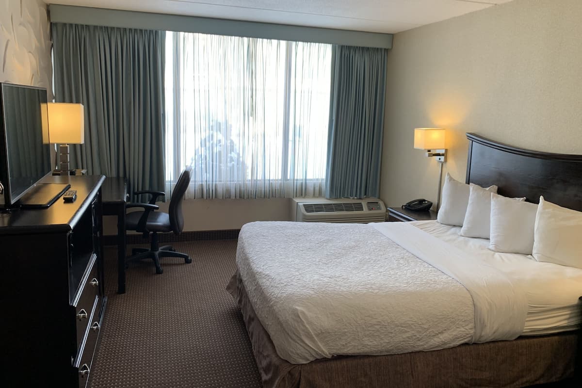 Une chambre d’hôtel avec un grand lit, un bureau avec une lampe, une chaise et une fenêtre avec des rideaux.