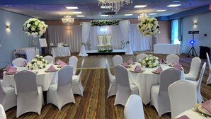 A banquet hall with round tables set for a formal event, featuring white chairs, gold table settings, and floral centerpieces.