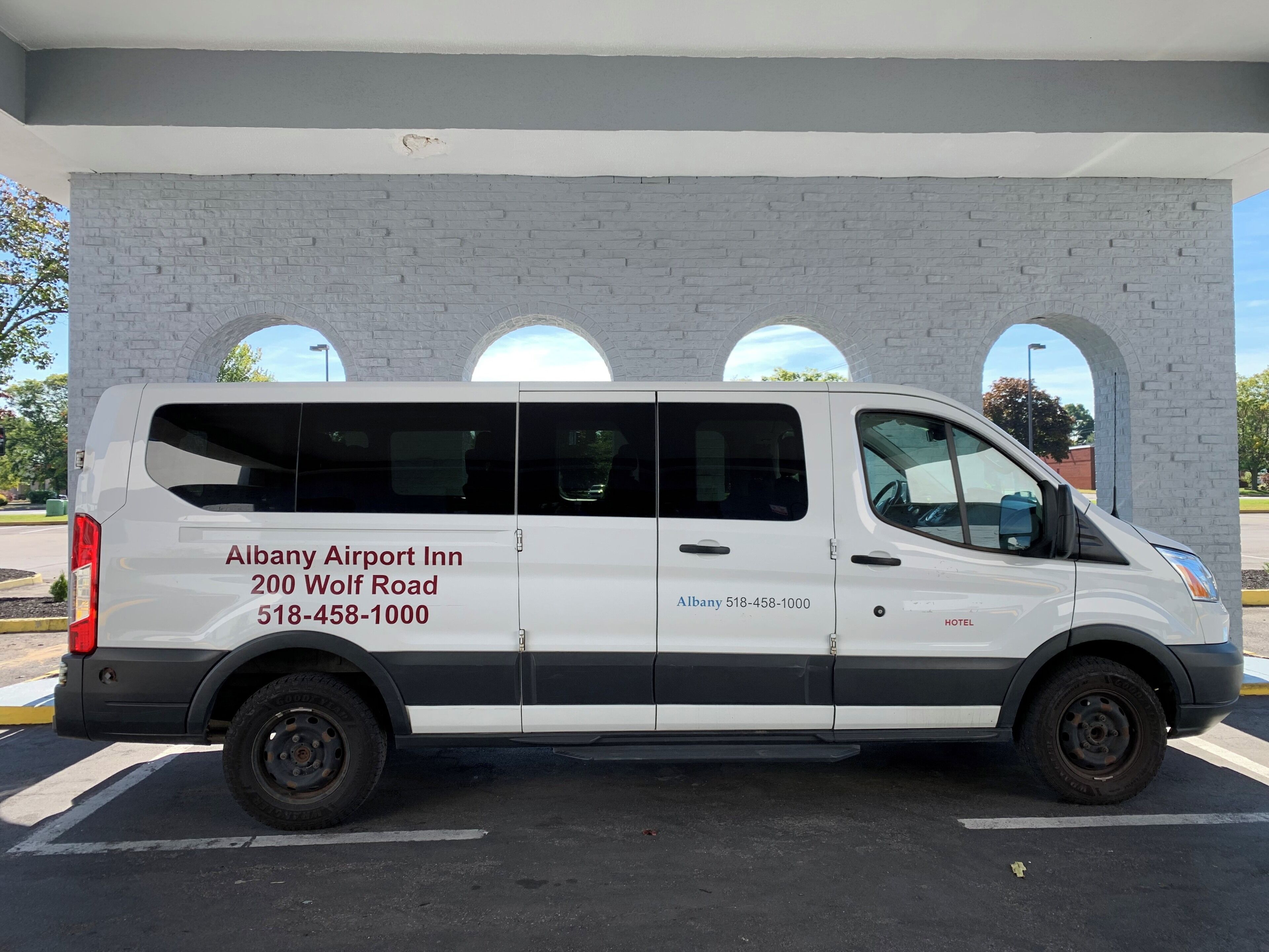 A white van parked in a parking lot with the text "Albany Airport Inn 200 Wolf Road 518-458-1000 HOTEL" on its side.
