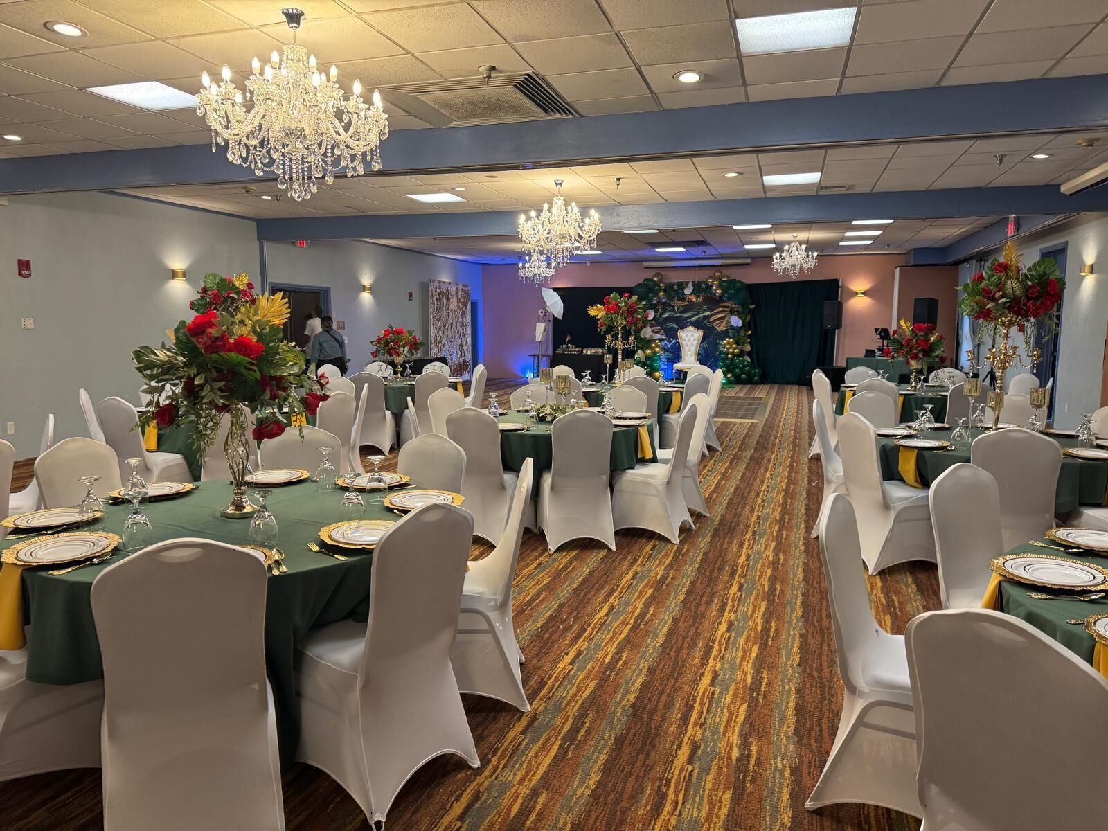 A banquet hall with round tables set for dining, white chairs, and chandeliers.