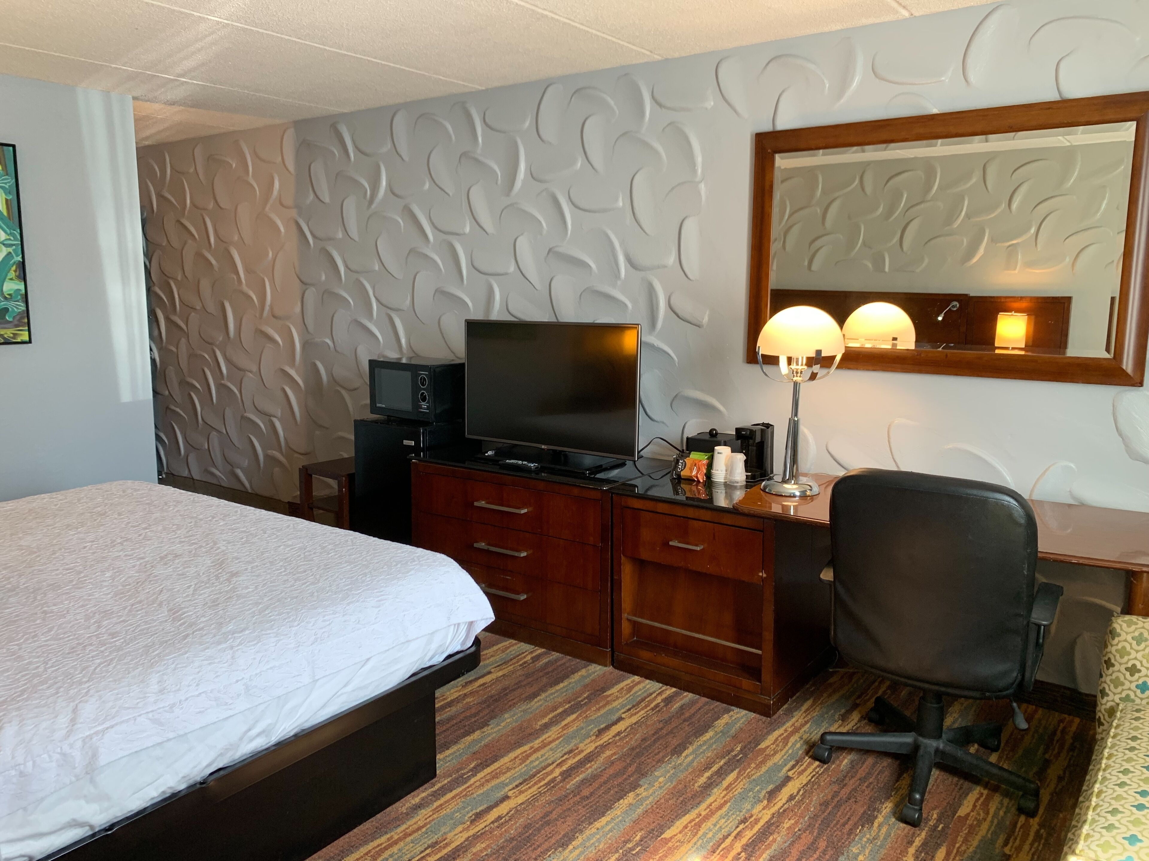 A hotel room with a bed, a desk with a computer, a television, and a mirror.