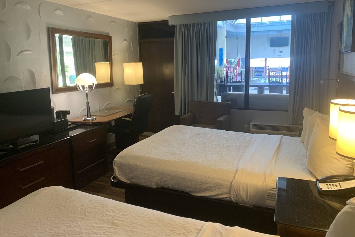 Une chambre d’hôtel avec deux lits, un bureau avec un ordinateur, une télévision et une fenêtre avec des rideaux.