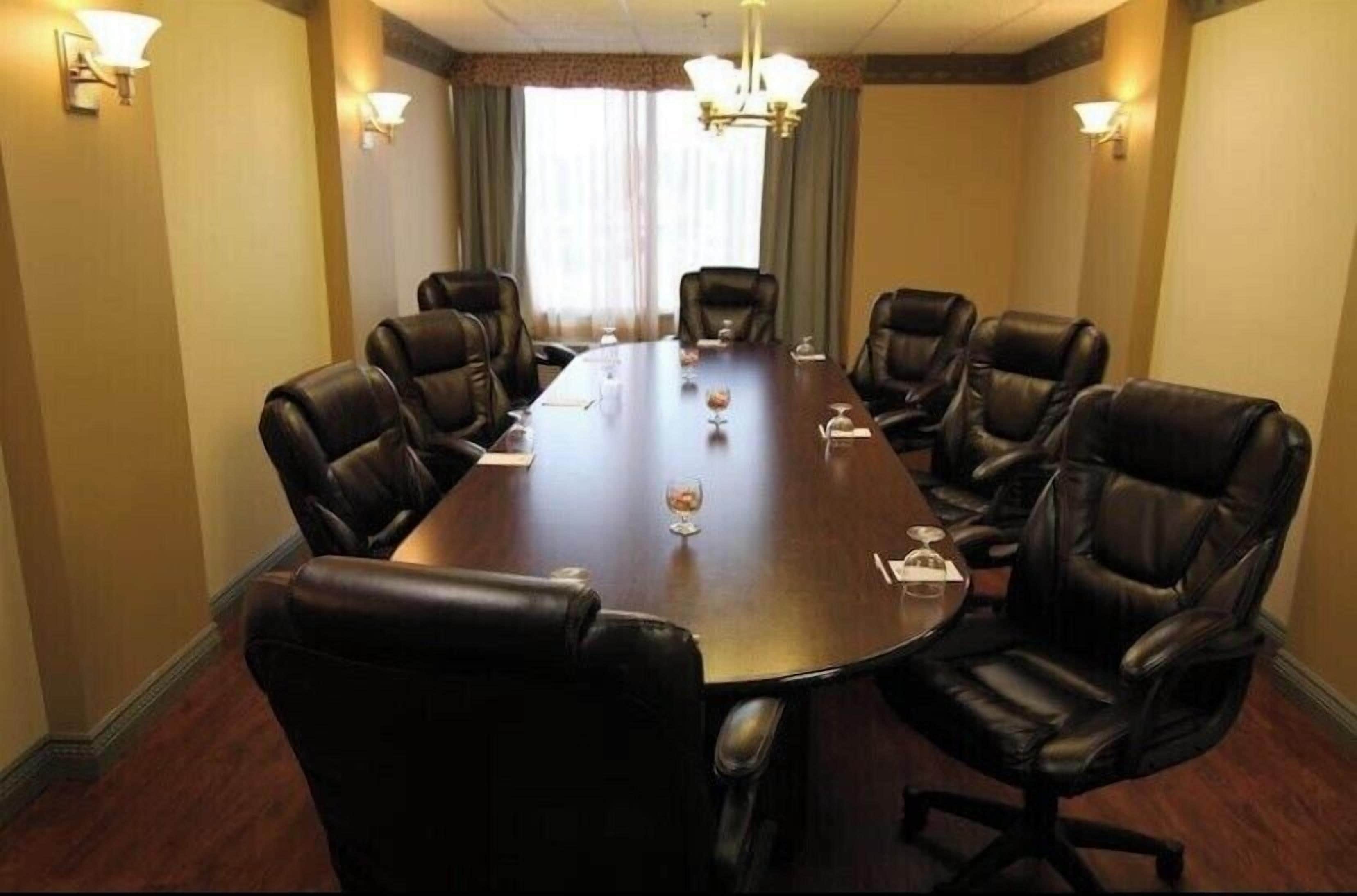 A conference room with a long table and six leather chairs, equipped with nameplates and glasses.