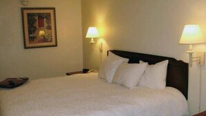 A hotel room with a large bed, two bedside lamps, a nightstand, a framed picture on the wall, and a telephone on the nightstand.