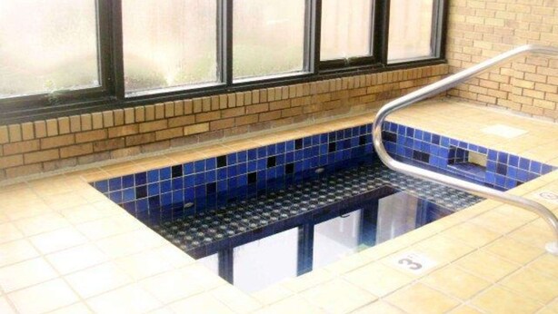 A pool area with a blue tiled floor, a metal handrail, and a window with a view of the outside.